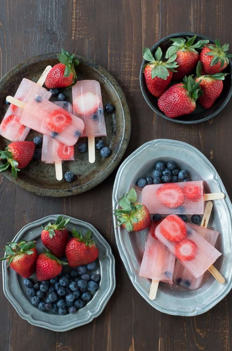 OneCrazyHouse Stay Cool without a pool 4 plates from overhead. Two long oval plates with popsicles made from cut berries and lemonade, 2 small plates with whole strawberries and blueberries