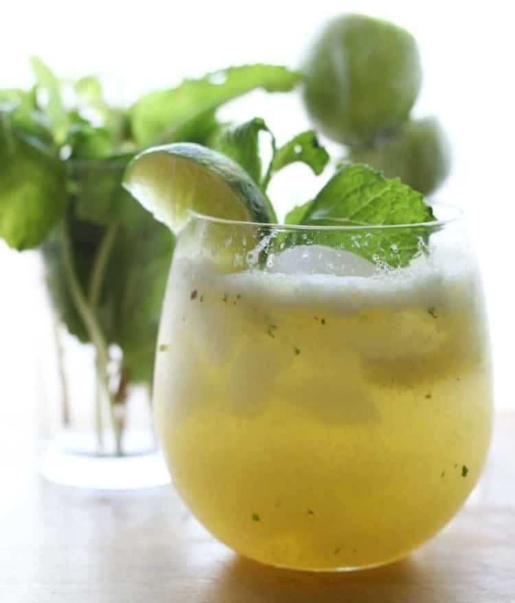 Glass of a pineapple No-Jito garnished with a lemon wedge and mint. 
