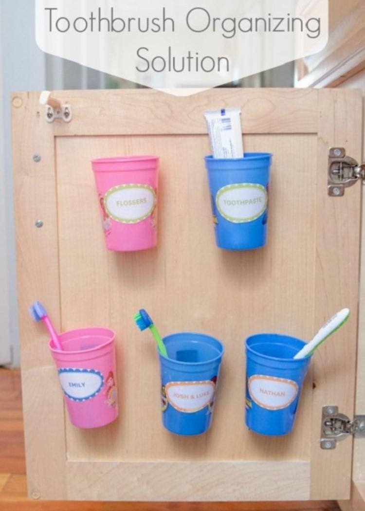 Pink & blue cups hang on inside of cabinet door to keep toothbrushes organized and clean. Fun idea for small kid's bathroom. 