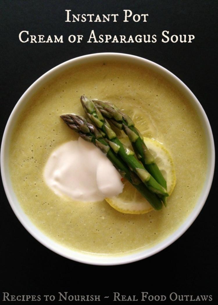 Cream of Asparagus Soup in white bowl, garnished with cooked asparagus, dollop of cream and slice of lemon, with black background.