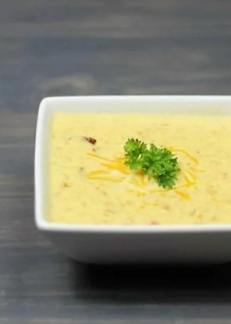 Low Carb Loaded Cauliflower Soup - a square bowl of cauliflower soup with bacon, cream cheese and cheddar cheese, garnished with parsley and shredded cheese.