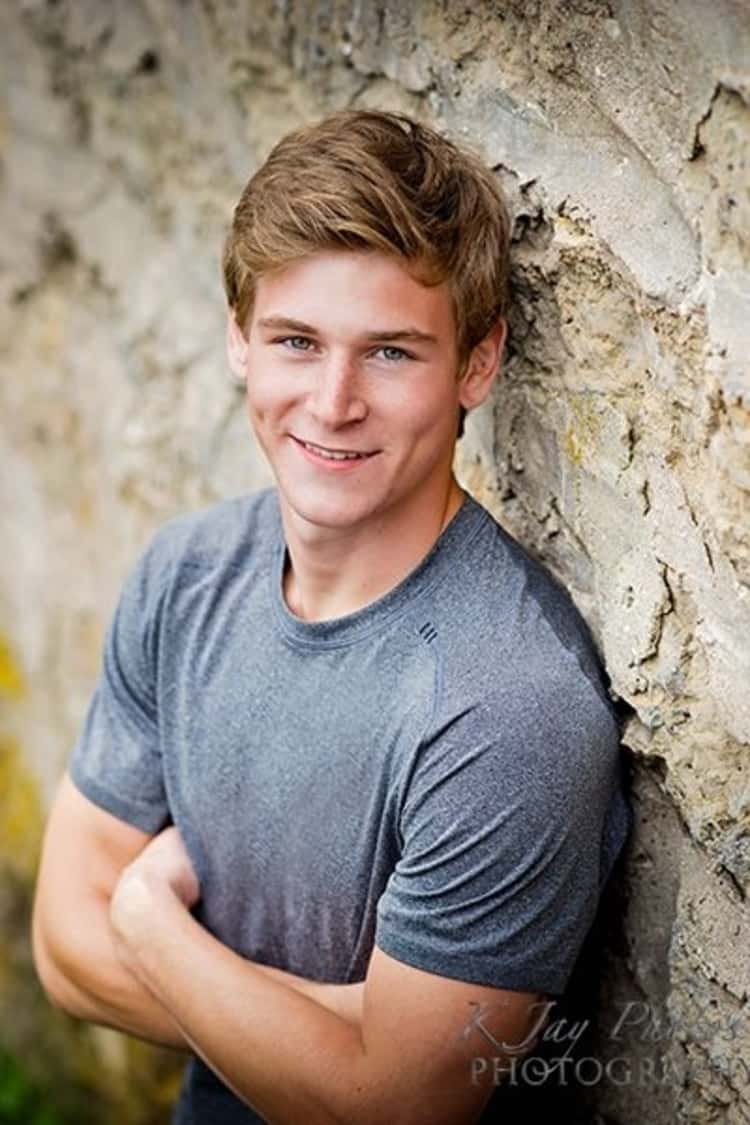senior picture ideas for guys - guy wearing a gray t-shirt and posing in front of a rugged wall