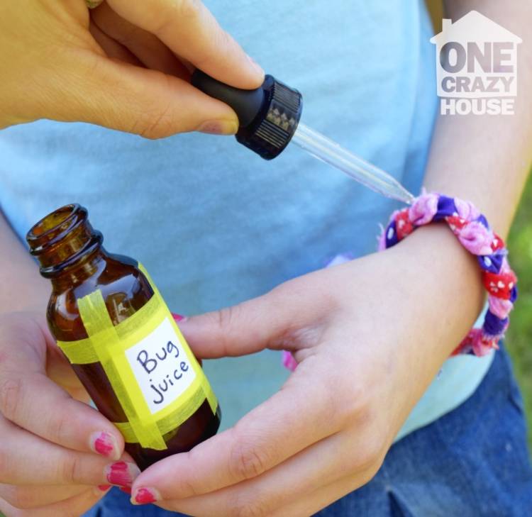 Genius essential oils tips and tricks - image of a child holding a glass bottle that says, "bug juice," while an adult applies essential oils to the child's fabric diffuser bracelet with a dropper