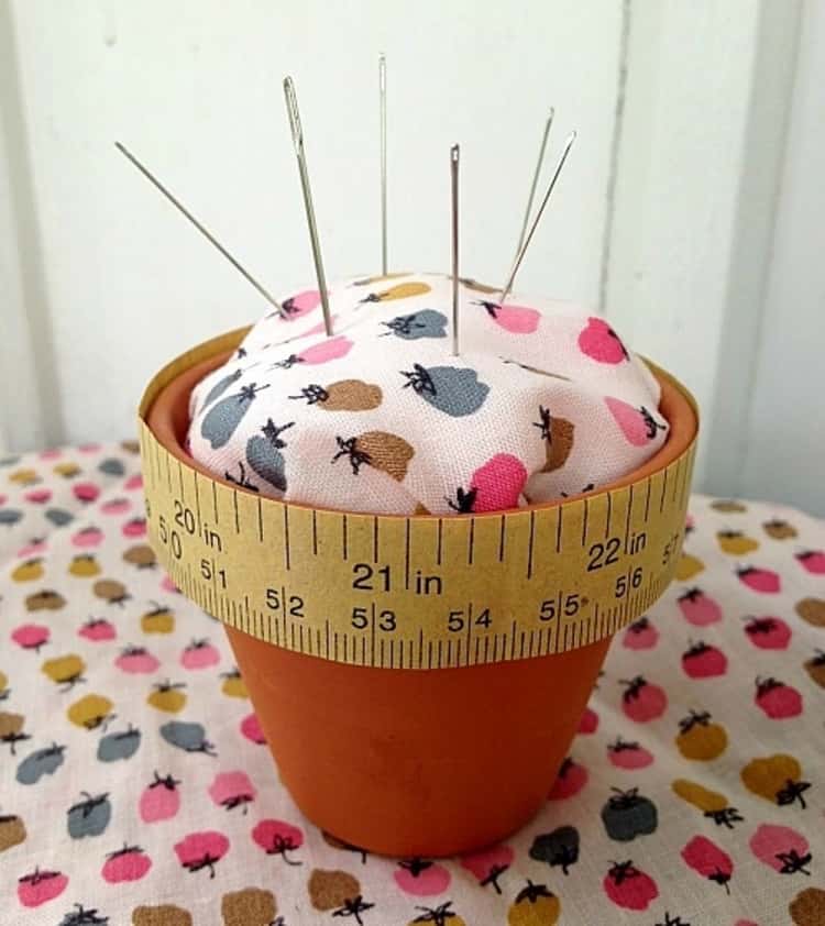 A pincushion made of a flowerpot and some fabric with pins and needles sticking out of the cushion