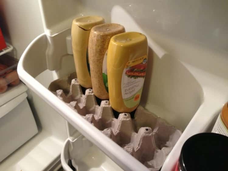 Condiments stored upside down in fridge door compartment using egg carton as support 