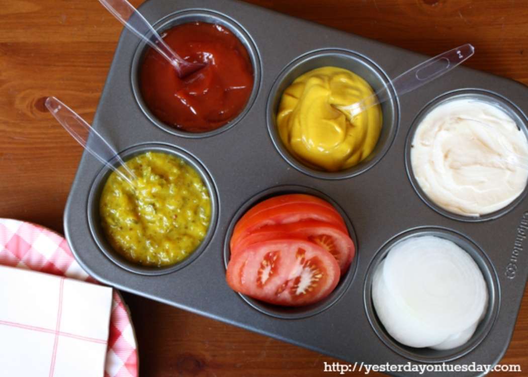 Brilliant Cookout Hack- Cupcake pan with different condiments and serving spoon in each of the cup spaces