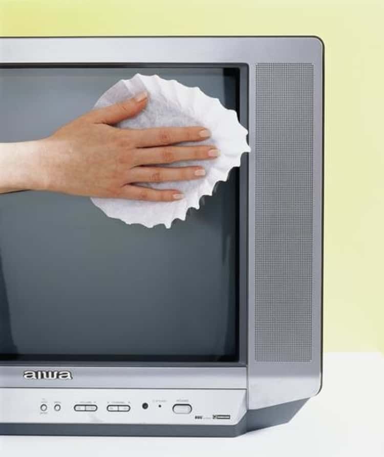 dusting hacks - person's right hand seeing using a coffee filter to wipe a TV screen 