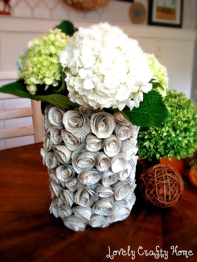 an empty oatmeal container decorated with paper flowers on the outside serving as a vase for flowers.