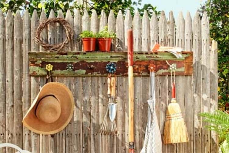 DIY garden tool rack with tools hanging from it and flower pots on top. 