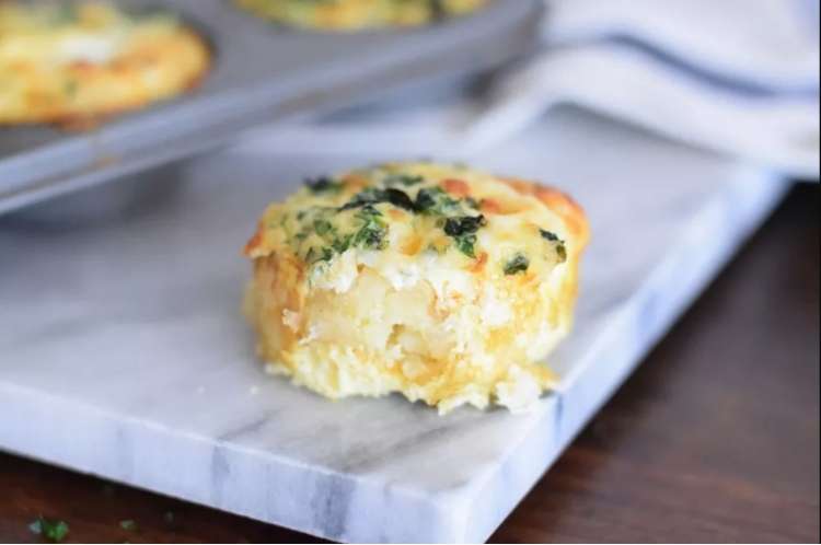 Counter with a hashbrown bite muffin on it, with cheese and  green vegetable showing