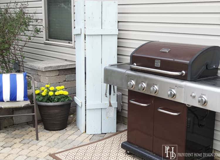 clever organization ideas with a DYI white shutters (outdoors) hiding an ugly water meter against the house. A grill next to the shutters.