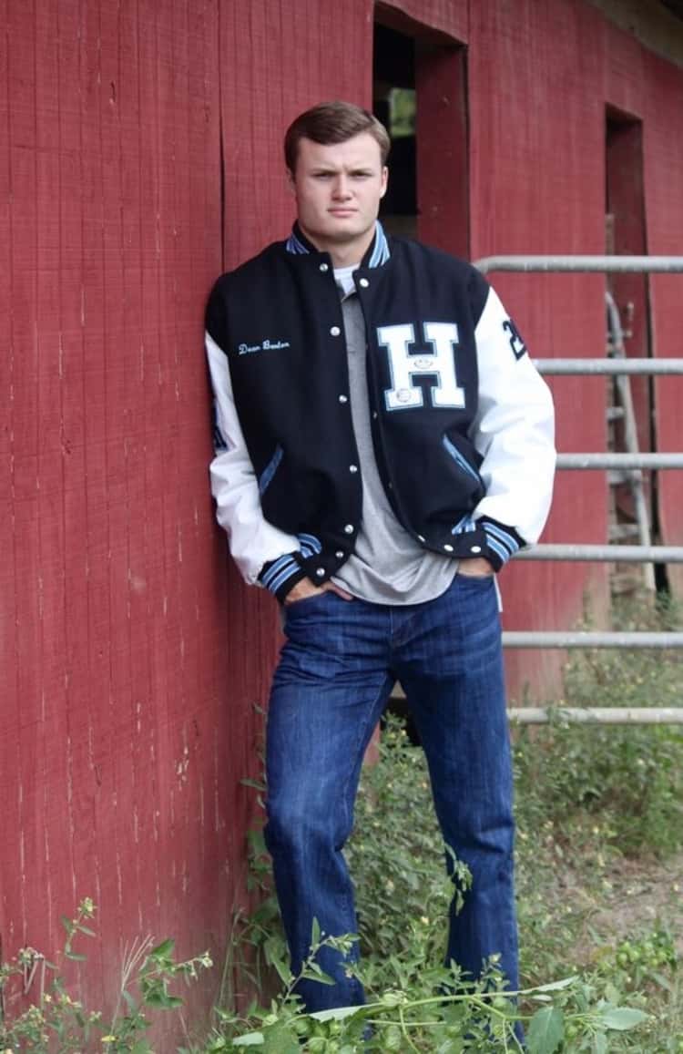 senior picture ideas for guys - guy in a Letterman jacket, t-shirt, and jeans posing in front of a barn. 