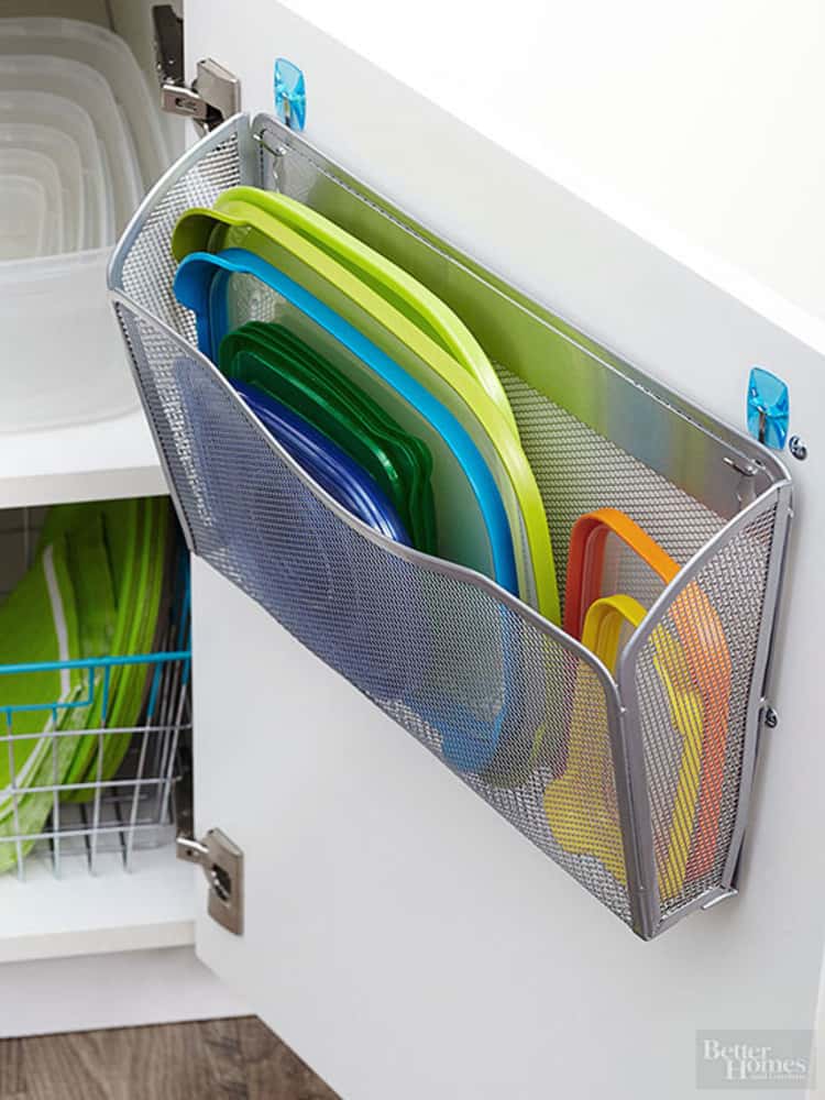 assorted Tupperware lids stored in a magazine holder mounted on a cabinet door 