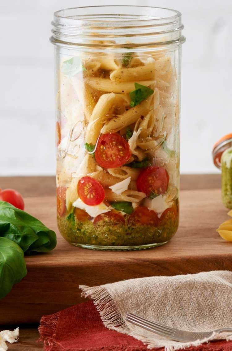 Pasta to go: jar with penne pasta noodles, red cherry tomatos, and green vegetables,