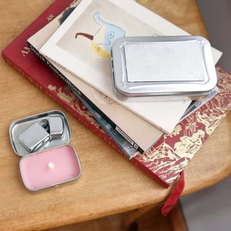 DIY candle on the left side made from an empty altoid tin and a lighter on top, with a stack of books on the right side. they're all sitting on a table.