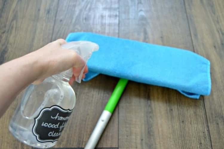 mopping tips - person's hand holding spray bottle and spraying cleaning solution onto mop covered with a microfiber cloth