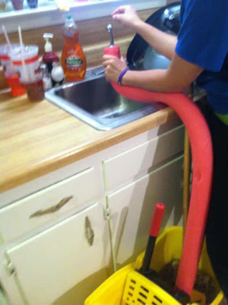 person using pool noodle to funnel water from kitchen sink into mop bucket