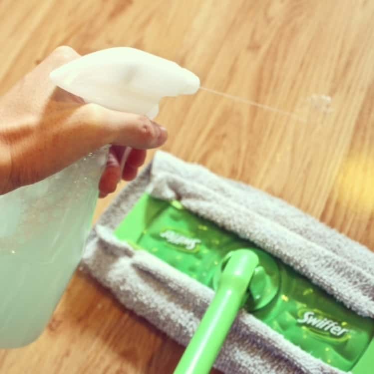 person's hand seen spraying cleaner on laminate floor 