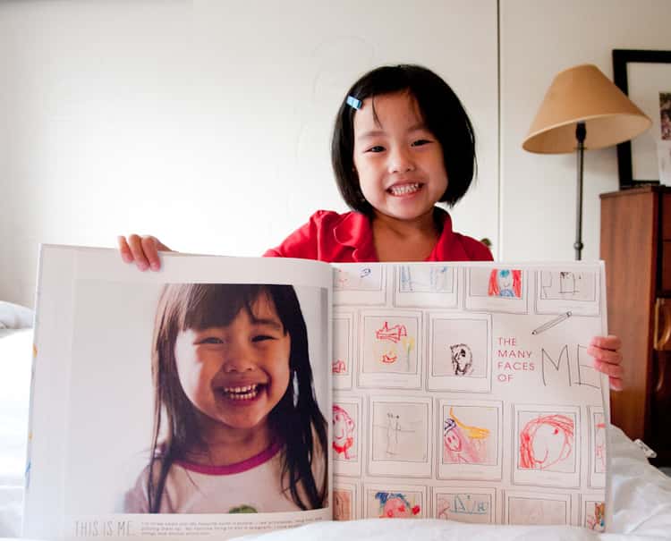 little girl holding a photo book with her on one page and her artwork on another