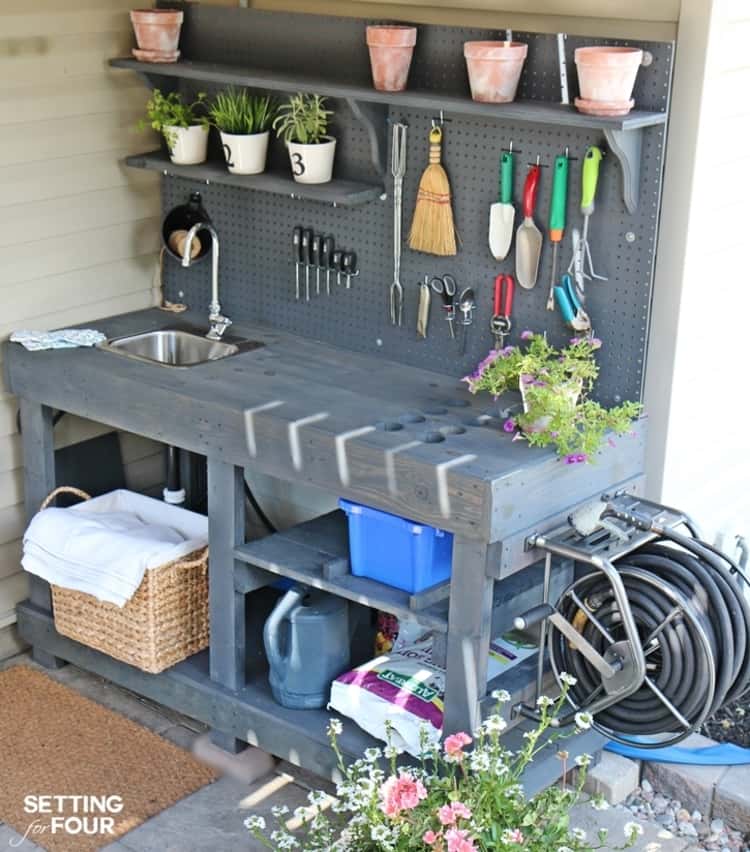 DIY potting bench with pots, a sink with faucet, hose mounted to the side, and a pegboard with hooks to hold garden tools