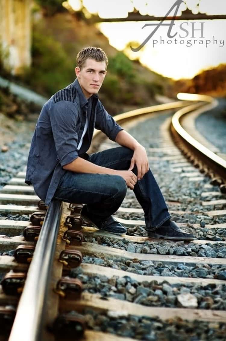 senior picture ideas for guys - guy posing for a photo while seating on an empty railroad track