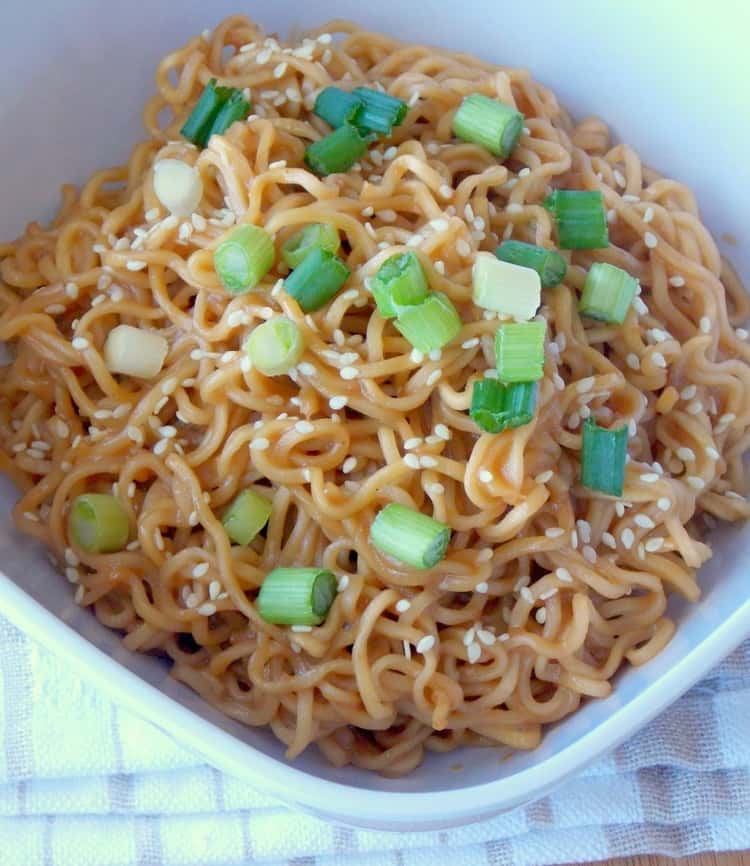 A plate of ramen noodles tossed in peanut butter sauce and topped with some sesame seeds and green onions