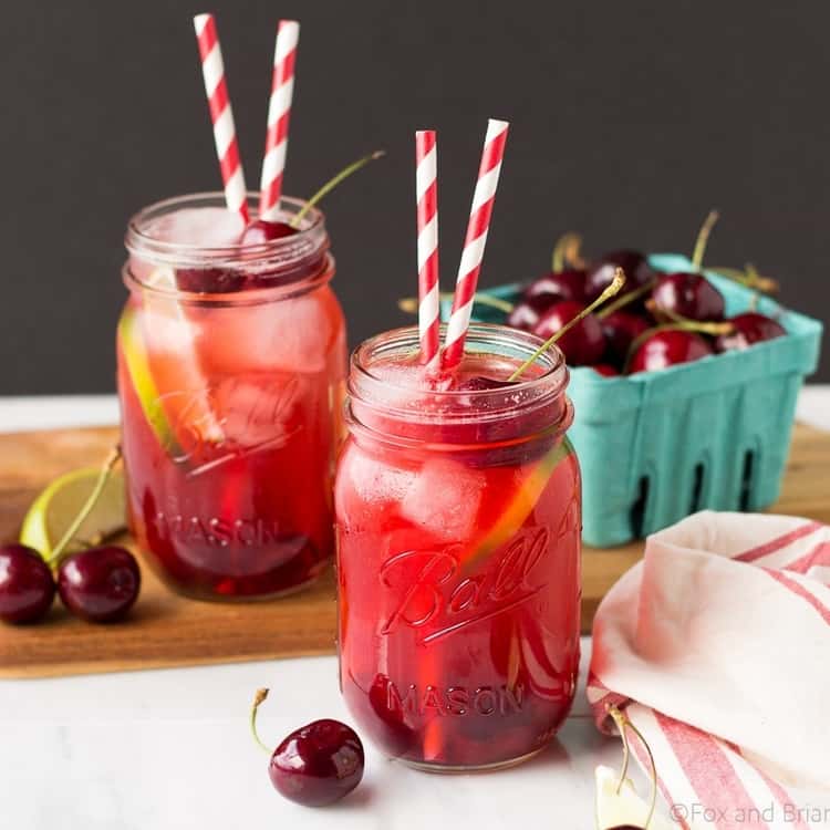 2 Sparkling Cherry Limeade mocktails garnished with some cherries and lime wedges. 