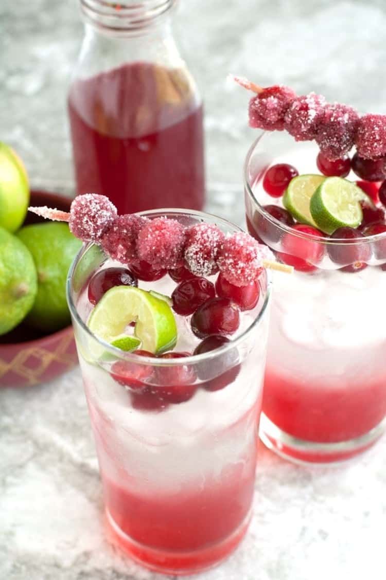 2 glasses of garnished Sparkling Cranberry Lime Mocktails and a glass bottle of cranberry syrup