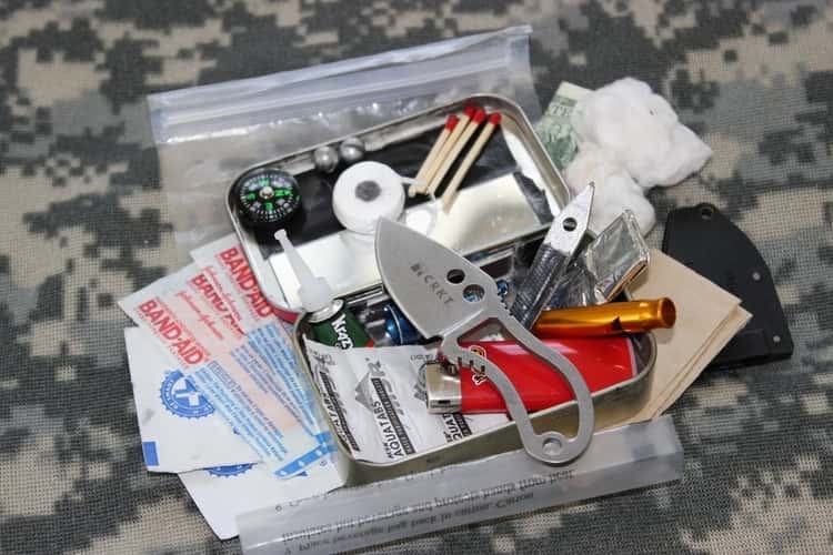 A survival kit with items for survival put inside an empty altoid tin, some items are on the outside of the tin.
