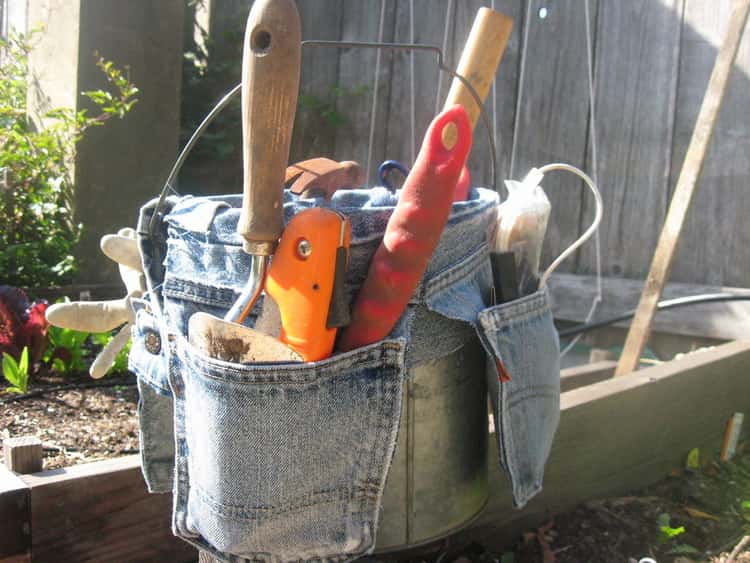 bucket with diy jeans cut and made into pocket that go around the bucket and it's holding garden tools.