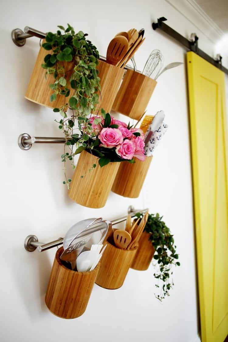 3 towel bars hanging on the wall on top of each other with canisters hung on them and utensils inside, a couple of them with flowers