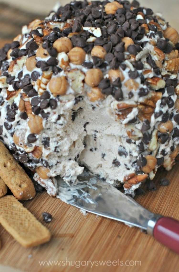 Turtle cheeseball on a wood board with a small knife, and a smal piece cut out of the front