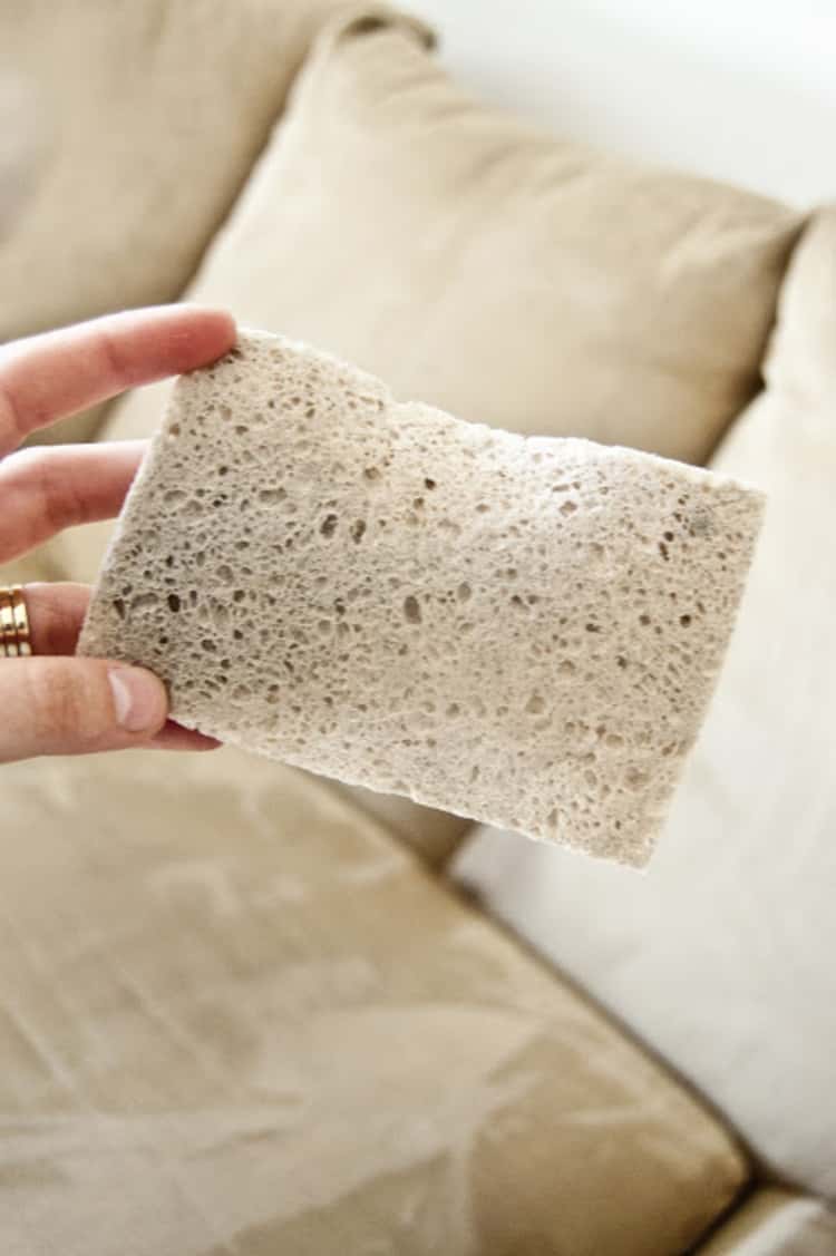 upholstery tips - person holding up dirty sponge and microfiber couch in the background