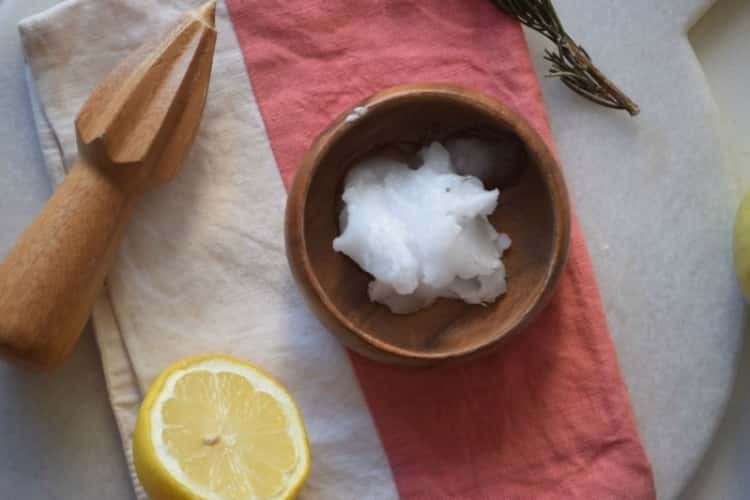 wood bowl with coconut oil in it, half a lemon next to it and a wood mixer on the side.