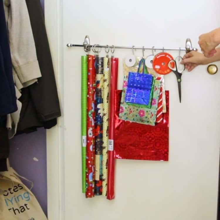 hanging wrapping paper, bags, ribbons, and scissors on a rod and hooks and rings on back of door of closet