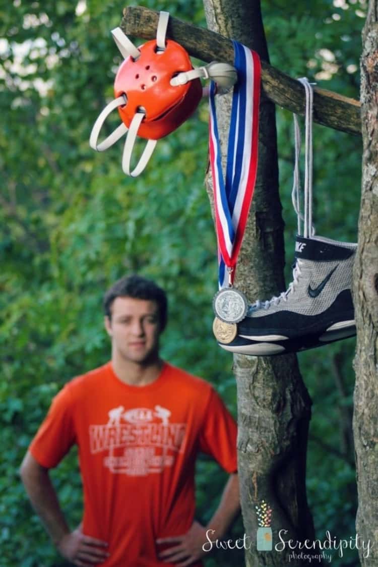 a wrestler's medals, helmet, and shoe hanging on a tree and a guy seen out of focus in the image