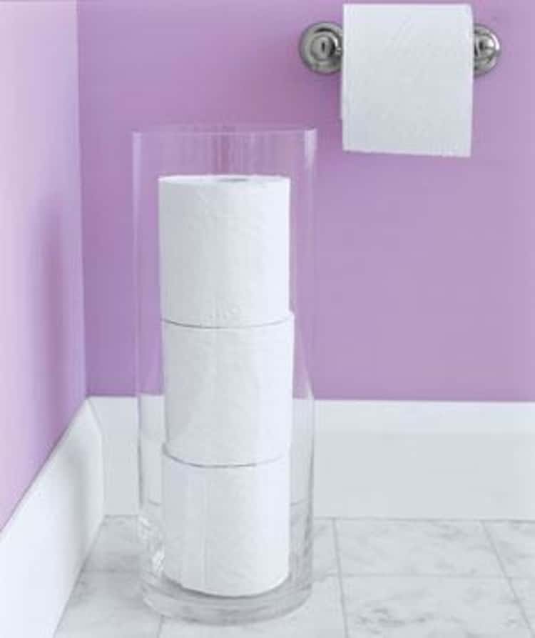 toilet paper storage in bathroom using a tall hurricane vase for elegant and clean look