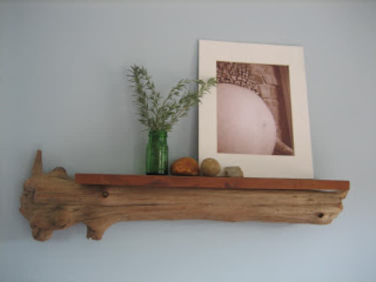 DIY driftwood floating rack with a shelf, a vase with green flowers, a white picture frame and some decorations