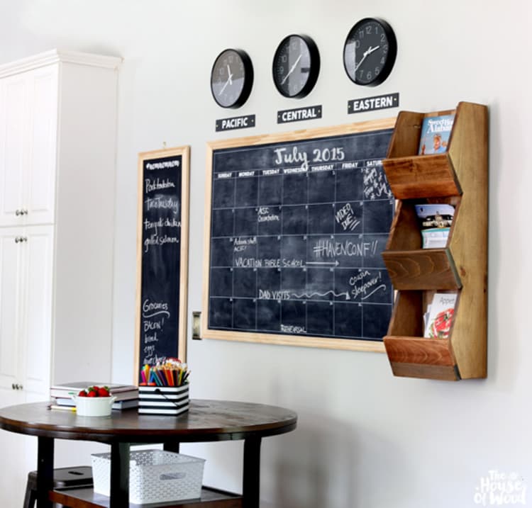 A Blackboard And A Cubby Shelf Command Center with mounted clocks and a tall blackboard on top and a small table with craft supplies in front