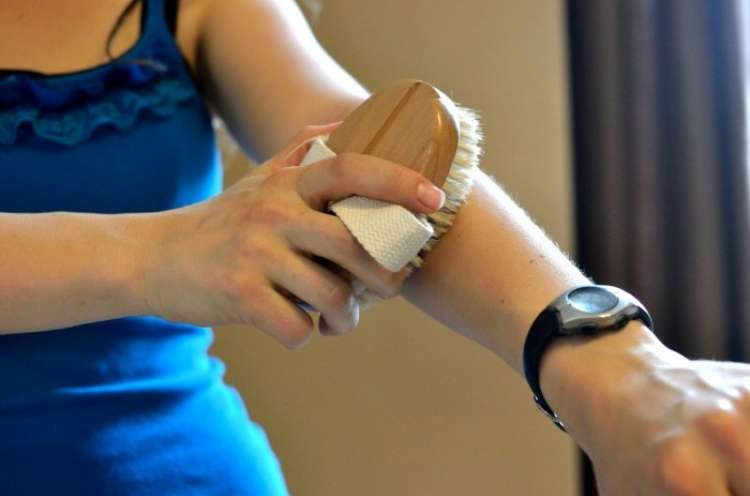 woman in a blue dress brushing her skin with a soft brush 