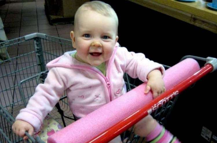 baby in shopping cart with handle covered with a pool noodle