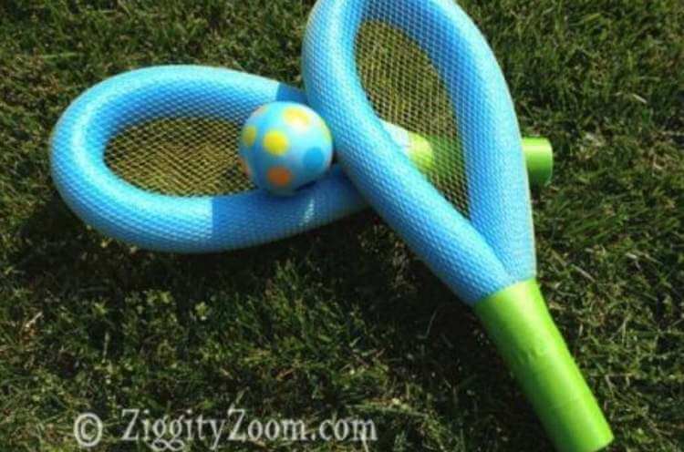 DIY uses for pool noodles- a racket and ball set made from pool noodles, netting, and tape resting on the grass