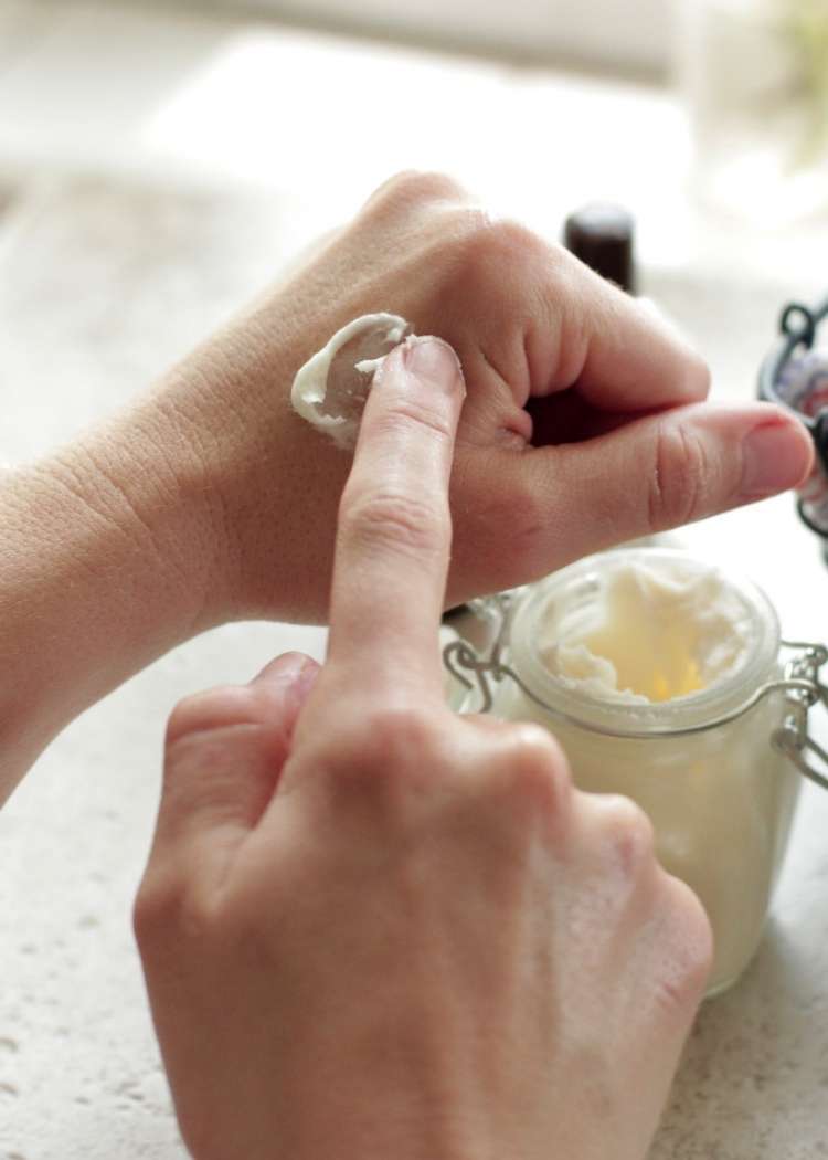 a hand rubbing some cream on her other hand with a cream of jar in the background