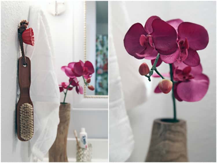 Using decorative knobs to hang items in the bathroom like a hair brush. there's a vase with maroon flowers too. 