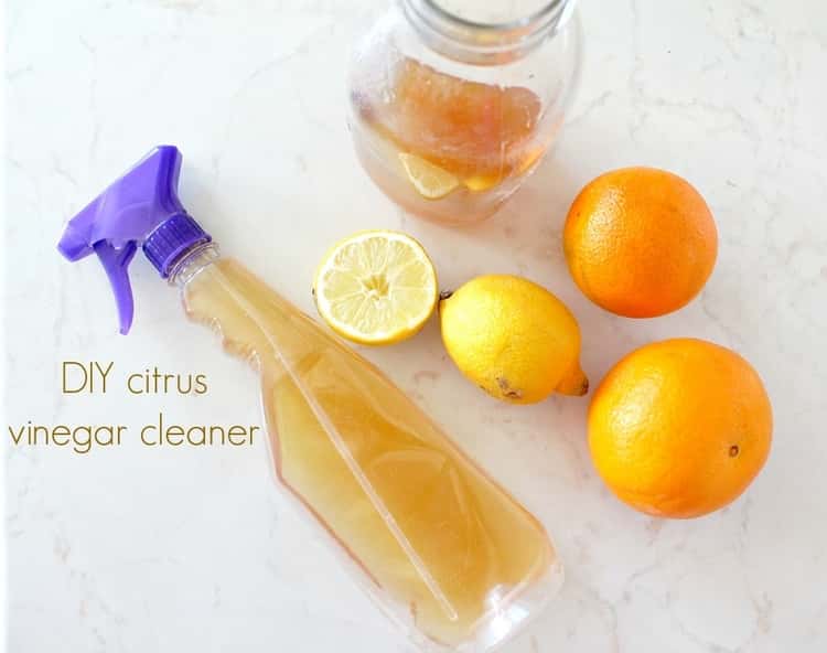 A spray bottle full of citrus vinegar cleaner, a jar half full of citrus vinegar cleaner and some lemons.