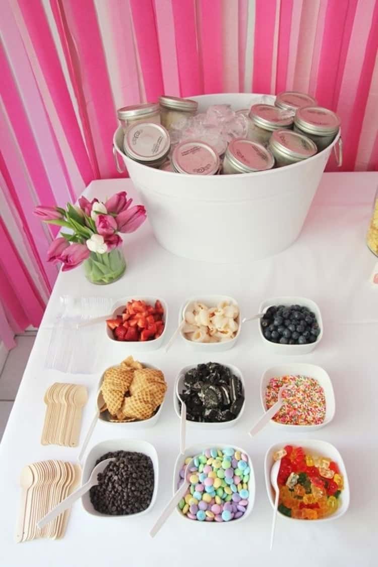 An ice cream sundae bar with pre-scooped ice cream in small mason jars and an array of favorite ice cream toppings like sprinkles, fruits and candies