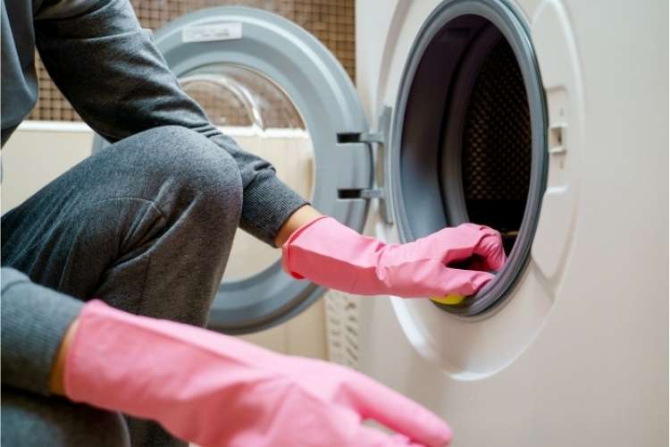 OneCrazyHouse Spring Cleaning Person wearing cleaning gloves kneeling in front of open washing machine