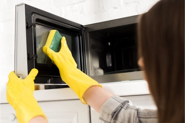 OneCrazyHouse how to clean microwaves woman wearing gloved cleaning a microwave