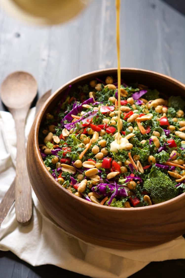 Rainbow kale salad with a fresh peanut Dijon dressing being drizzled on