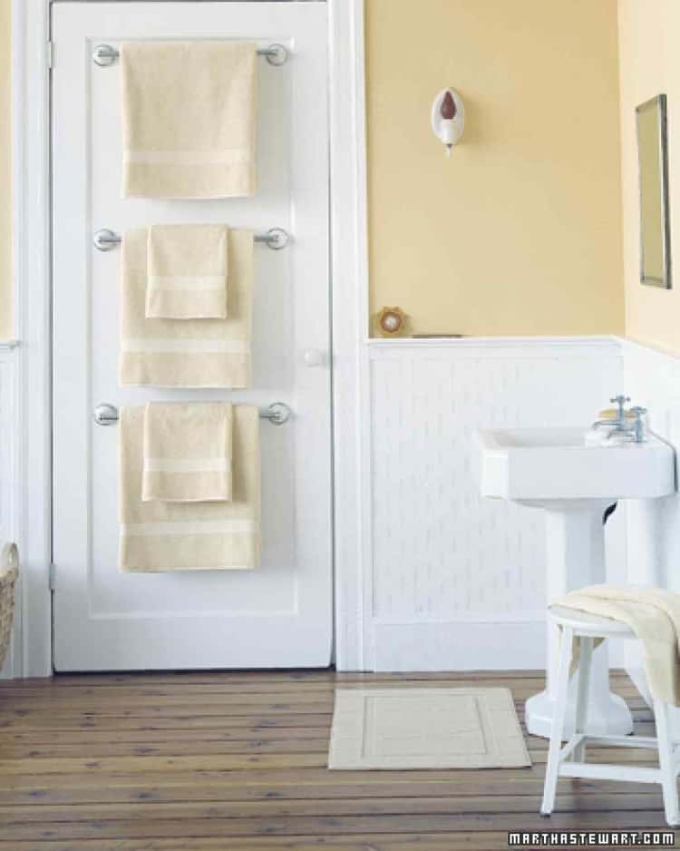 bathroom organizing tips with a Trio of towel bars on the back of the bathroom door and cream colored towels hanging from them